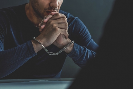 Criminal man with handcuffs in interrogation room.